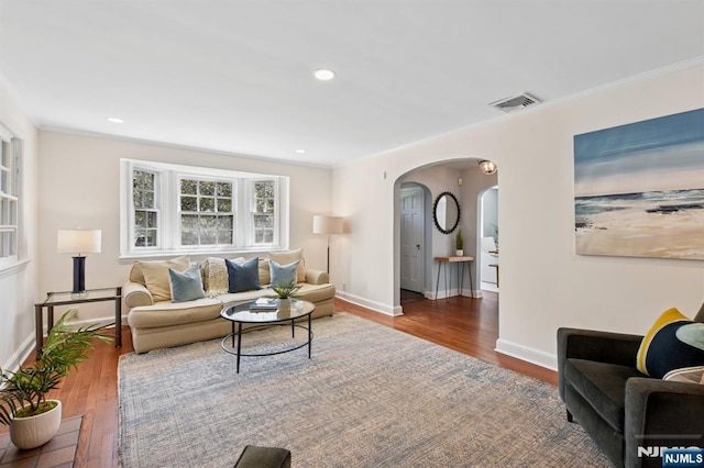 living area with crown molding, arched walkways, visible vents, and wood finished floors