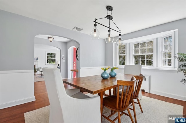 dining room featuring arched walkways, baseboards, wood finished floors, and visible vents