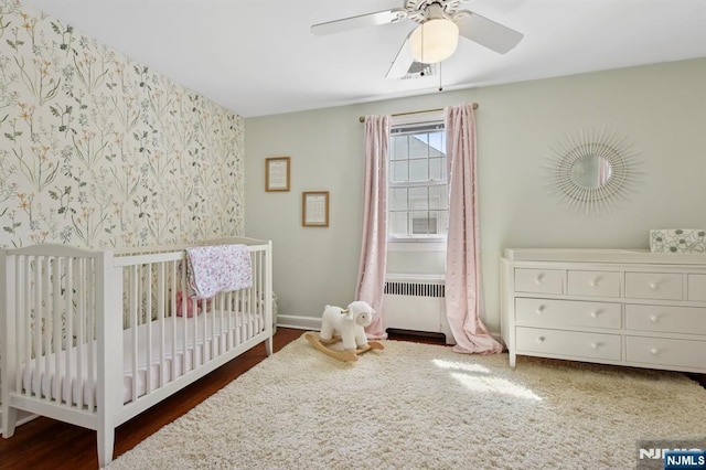 bedroom featuring visible vents, a nursery area, wood finished floors, baseboards, and radiator