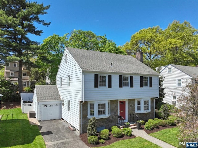 colonial inspired home featuring an outdoor structure, a garage, stone siding, a front yard, and a chimney