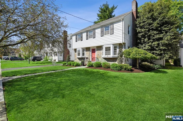 colonial house with a chimney, stone siding, and a front yard