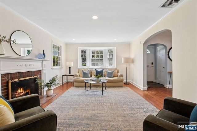 living area featuring visible vents, ornamental molding, arched walkways, and wood finished floors