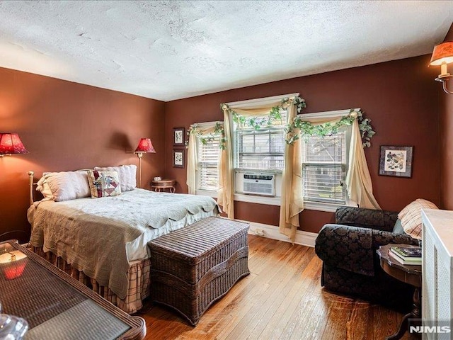 bedroom with baseboards, wood-type flooring, a textured ceiling, and cooling unit