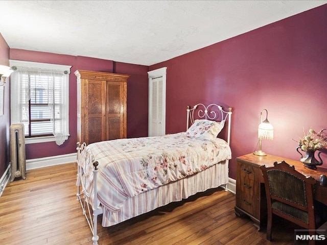 bedroom featuring radiator heating unit, baseboards, a closet, and wood finished floors