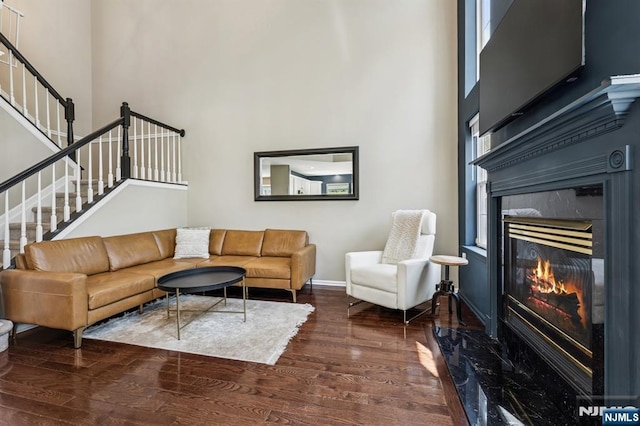 living room featuring a towering ceiling, a fireplace, wood finished floors, baseboards, and stairs