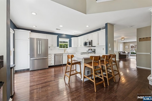 kitchen featuring dark wood-style flooring, light countertops, white cabinets, appliances with stainless steel finishes, and backsplash