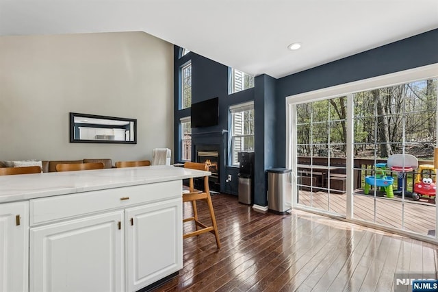 kitchen with dark wood-style flooring, light countertops, a warm lit fireplace, recessed lighting, and white cabinetry
