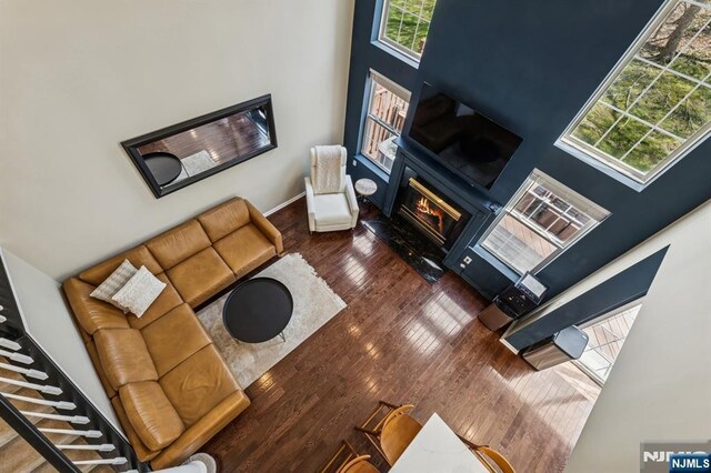 living area featuring wood-type flooring, a glass covered fireplace, a towering ceiling, and baseboards