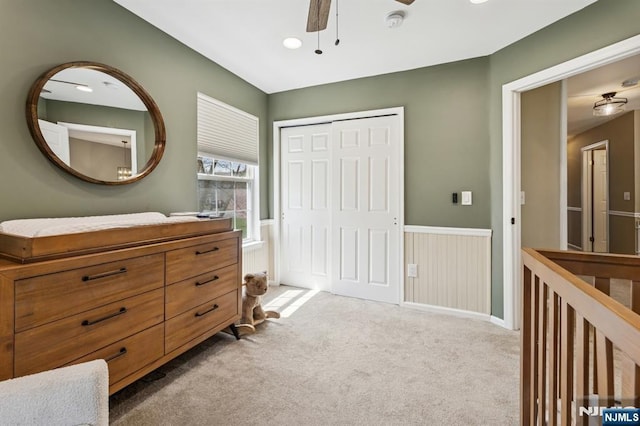 bedroom featuring a ceiling fan, light carpet, a wainscoted wall, and a closet