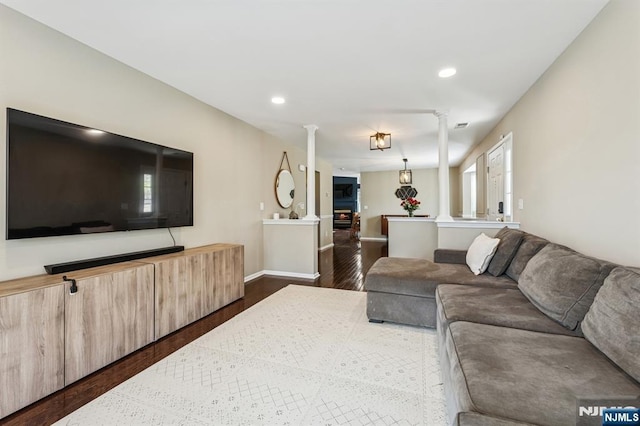 living room with recessed lighting, decorative columns, dark wood-style flooring, and a warm lit fireplace