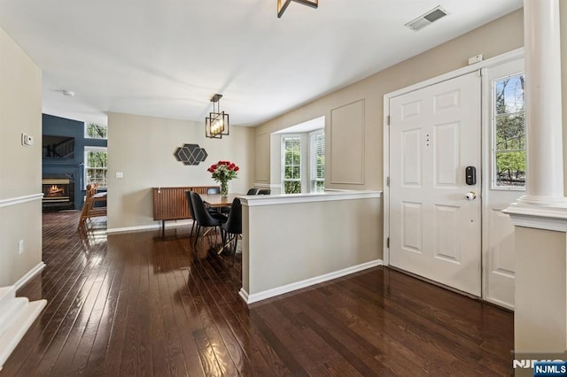 foyer with dark wood-style flooring, a lit fireplace, baseboards, ornate columns, and visible vents