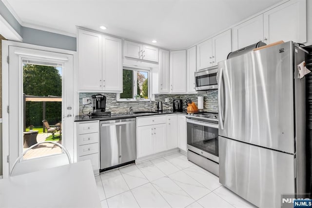 kitchen with dark countertops, a sink, stainless steel appliances, white cabinetry, and tasteful backsplash