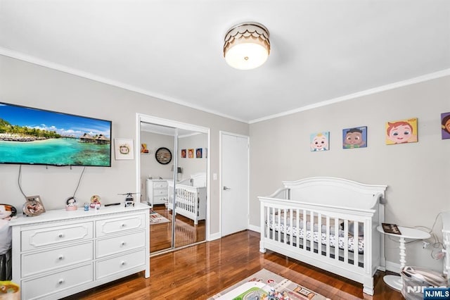 bedroom featuring crown molding, baseboards, a nursery area, and wood finished floors