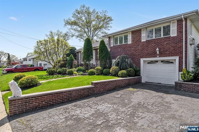split level home featuring a garage, driveway, brick siding, and a front yard