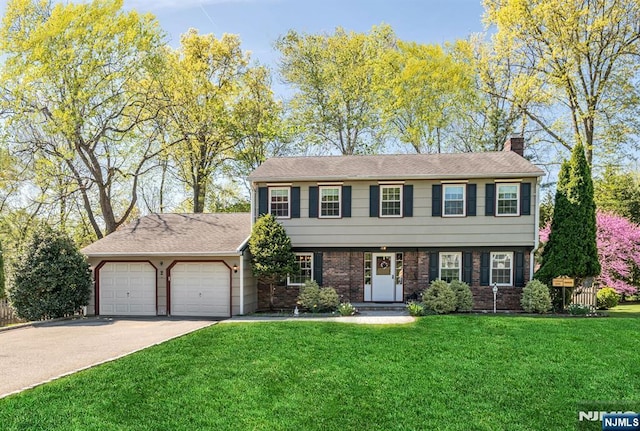 colonial house with a front lawn, a chimney, brick siding, an attached garage, and driveway