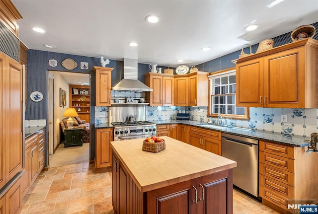 kitchen with a kitchen island, wall chimney exhaust hood, a sink, stainless steel appliances, and butcher block countertops