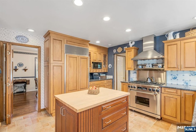 kitchen featuring wall chimney range hood, stone finish floor, backsplash, high quality appliances, and wallpapered walls