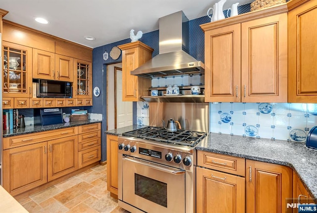 kitchen featuring black microwave, high end stove, tasteful backsplash, glass insert cabinets, and wall chimney exhaust hood