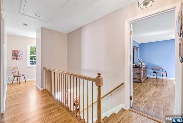 hallway featuring baseboards, an upstairs landing, wood finished floors, and attic access