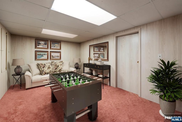 game room featuring wood walls, carpet flooring, and a drop ceiling