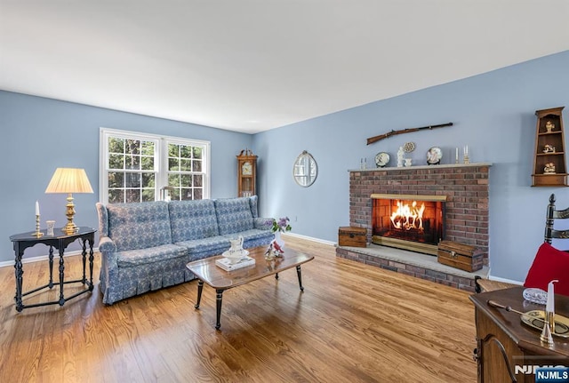 living room featuring baseboards, a brick fireplace, and wood finished floors