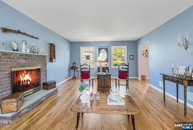 living area with baseboards, light wood-style flooring, and a brick fireplace