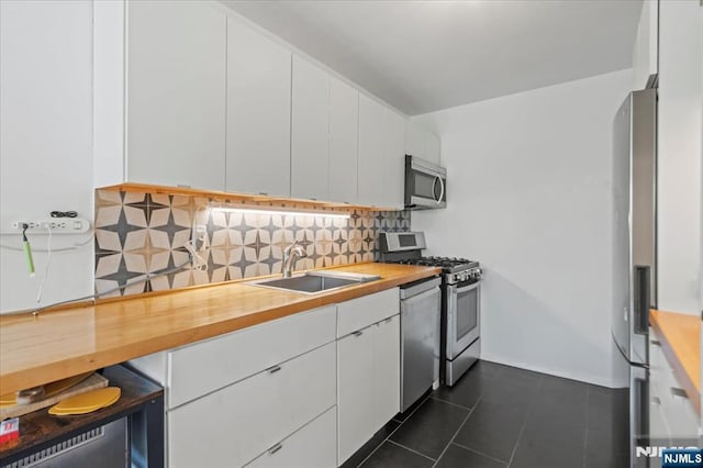 kitchen featuring white cabinets, a sink, wood counters, stainless steel appliances, and decorative backsplash