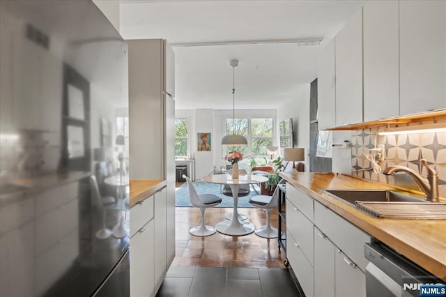 kitchen featuring a sink, wood counters, freestanding refrigerator, and white cabinetry