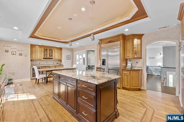 kitchen with crown molding, a raised ceiling, a kitchen island, built in refrigerator, and visible vents