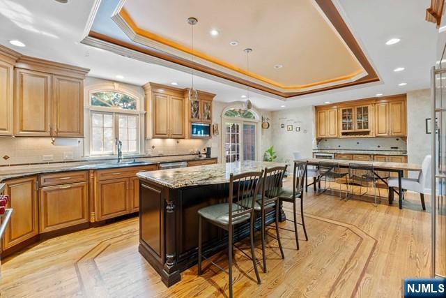 kitchen with crown molding, light stone countertops, a breakfast bar, a raised ceiling, and tasteful backsplash