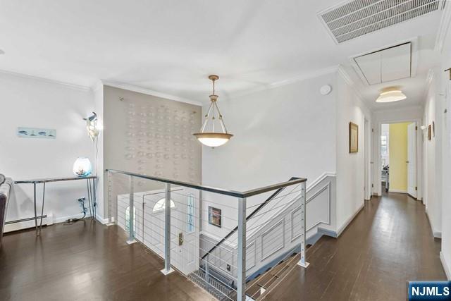 hallway featuring visible vents, ornamental molding, wood finished floors, attic access, and an upstairs landing