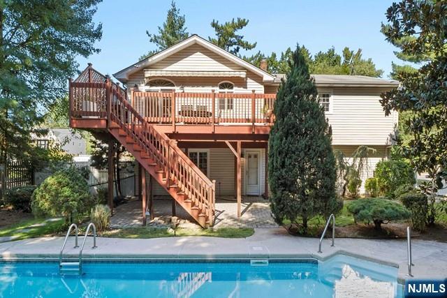 rear view of house with an outdoor pool, a wooden deck, stairway, and fence