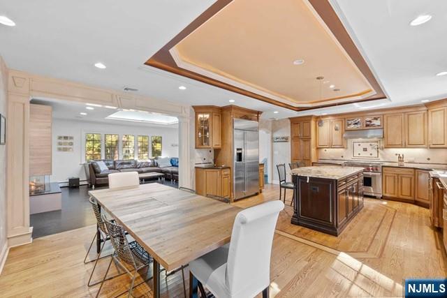 dining room with recessed lighting, ornamental molding, a raised ceiling, and light wood-style floors