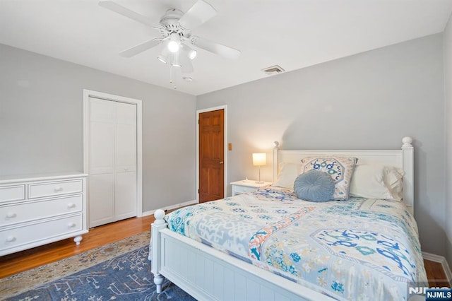bedroom featuring ceiling fan, visible vents, wood finished floors, baseboards, and a closet
