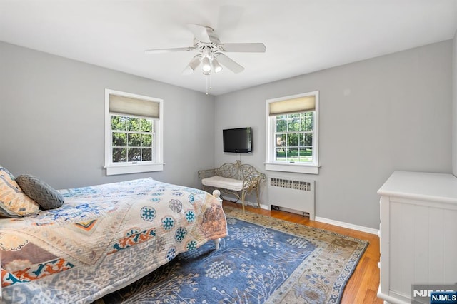 bedroom featuring multiple windows, radiator heating unit, and wood finished floors