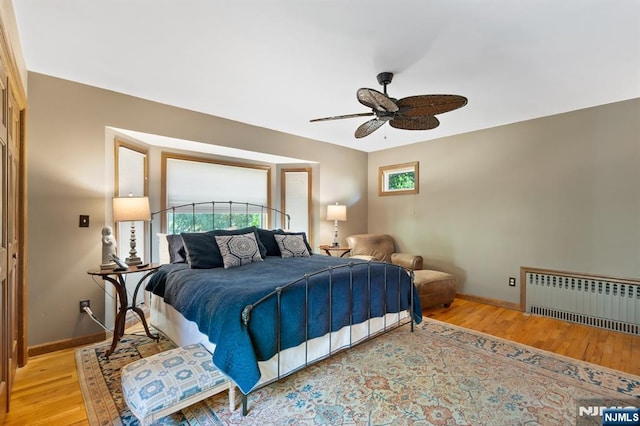 bedroom featuring baseboards, light wood-style flooring, and radiator