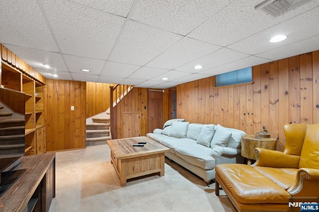 living room with light colored carpet, wood walls, a paneled ceiling, and stairway