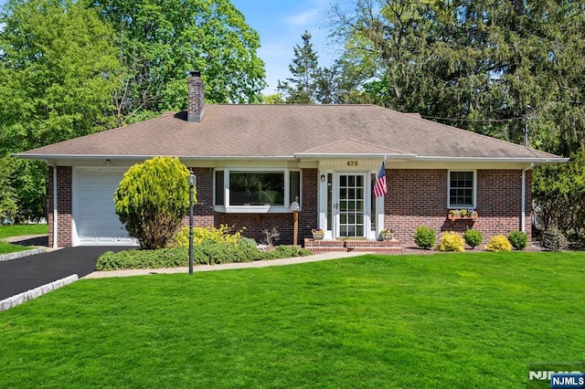 single story home with a front lawn, a chimney, brick siding, an attached garage, and driveway