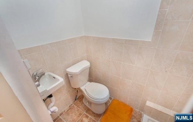 half bathroom featuring a sink, tile walls, tile patterned flooring, and toilet