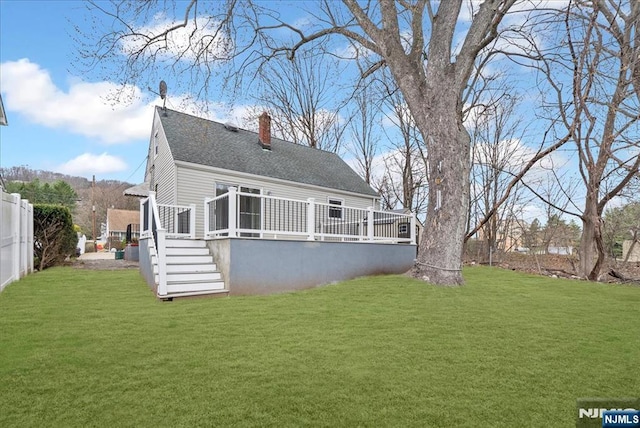 rear view of house featuring fence, a wooden deck, a chimney, and a lawn