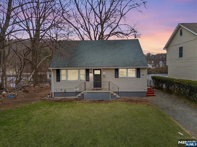 view of front of house with a yard and a shingled roof