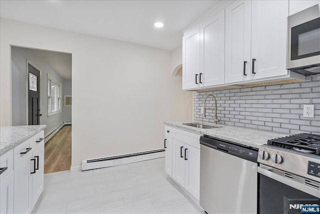 kitchen featuring appliances with stainless steel finishes, light stone counters, a sink, baseboard heating, and backsplash