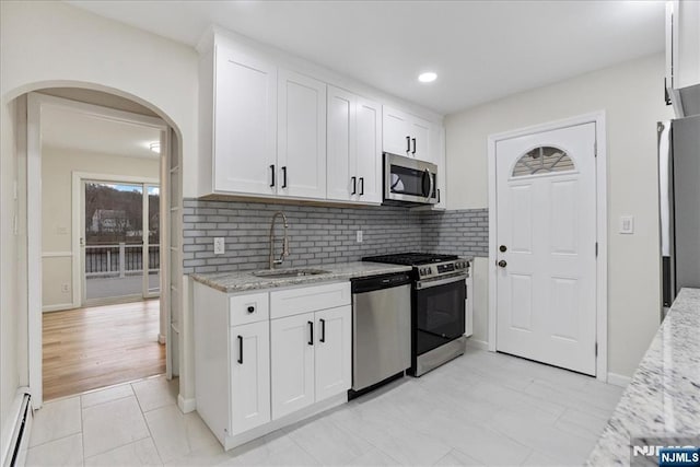kitchen with light stone countertops, arched walkways, a baseboard heating unit, a sink, and appliances with stainless steel finishes