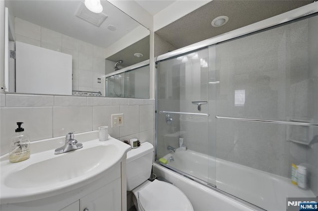 full bathroom with shower / bath combination with glass door, vanity, toilet, tile walls, and backsplash