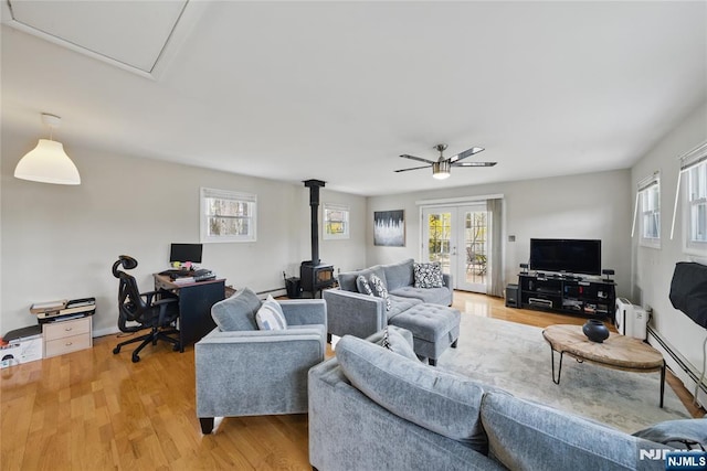 living area with ceiling fan, a wood stove, french doors, light wood-type flooring, and a baseboard heating unit