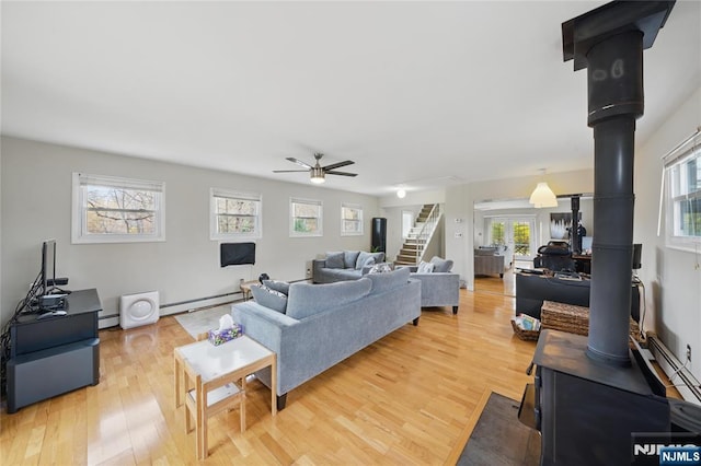 living area with a wood stove, light wood-style flooring, a ceiling fan, a wealth of natural light, and a baseboard radiator
