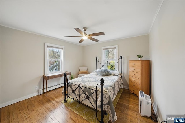 bedroom with crown molding, ceiling fan, baseboard heating, hardwood / wood-style floors, and baseboards