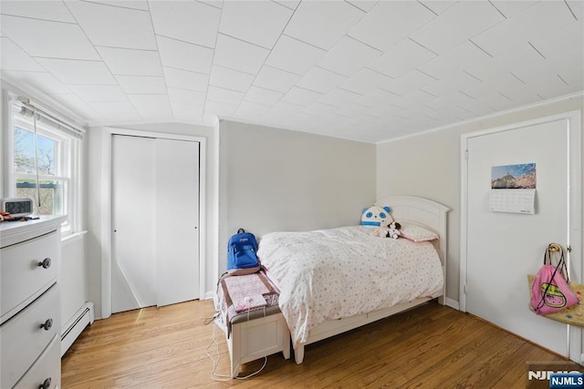 bedroom featuring a closet, baseboard heating, and light wood-type flooring
