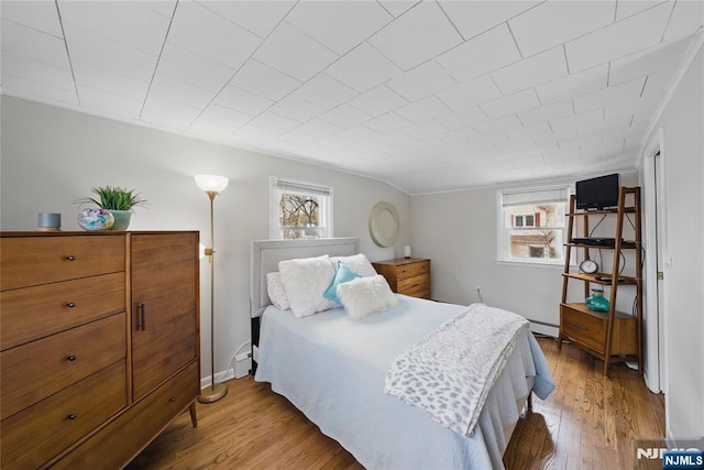 bedroom featuring wood finished floors, a baseboard heating unit, and multiple windows