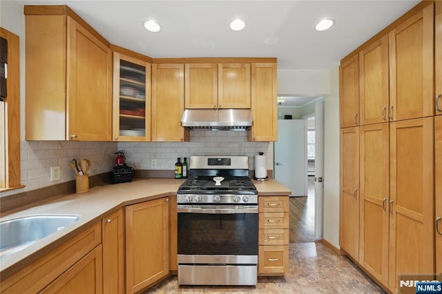 kitchen featuring decorative backsplash, light countertops, stainless steel gas range, glass insert cabinets, and under cabinet range hood